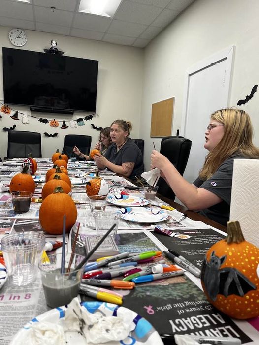 Religion students sit around a conference table painting pumpkins